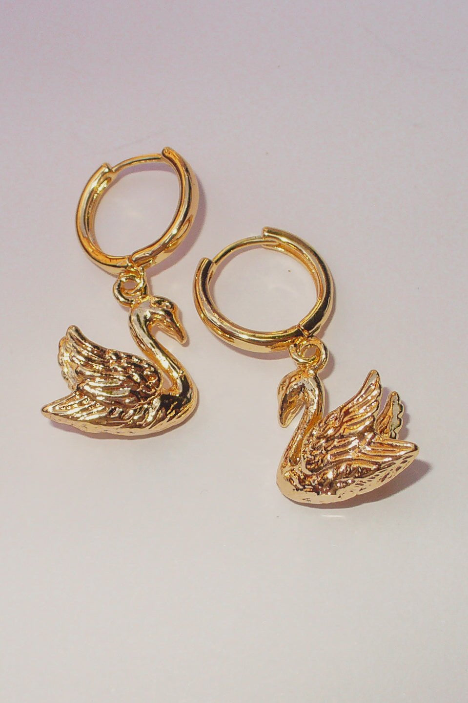Pair of gold swan charm huggie earrings on 16mm mini hoops