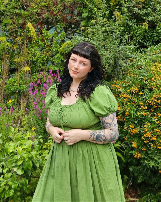 Woman in a green dress standing in a garden with trees and flowers in the background