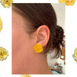 Close-up of an ear wearing a yellow floral earring with decorative yellow flowers around the image.